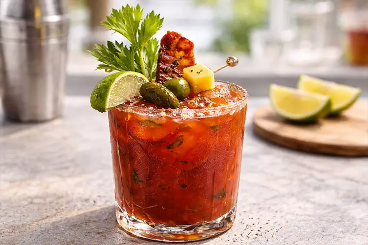 A Bloody Mary garnished with celery leaves, lime and olives
