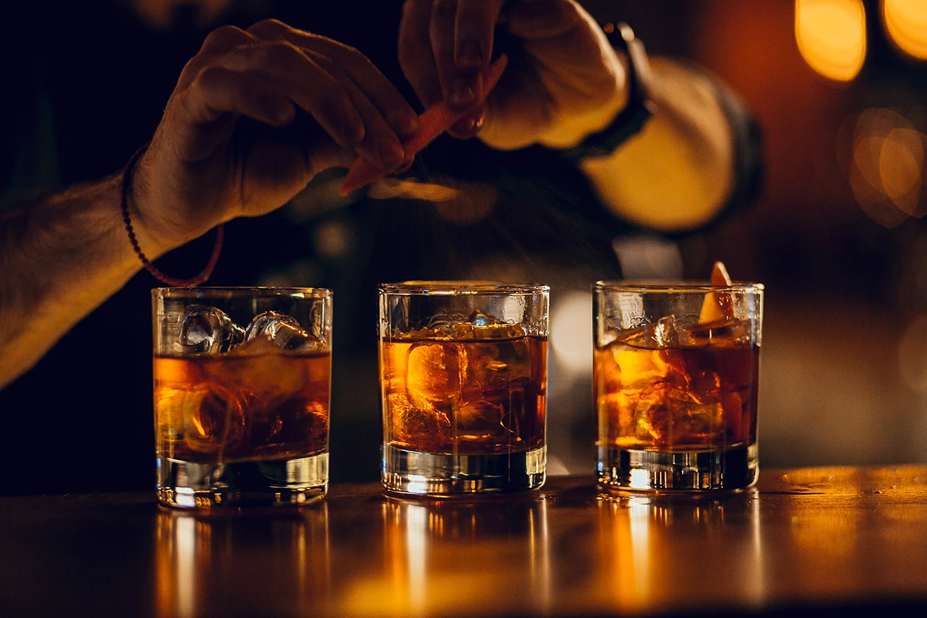 Three glasses of whiskey on ice lined up on a bar