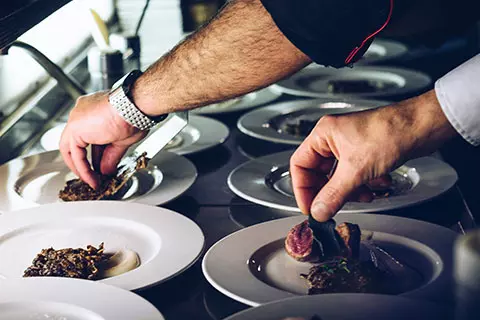 A chef plating a row of dishes on white plates
