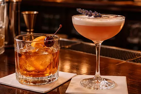 An old fashioned and a frothy pink cocktail on a bar
