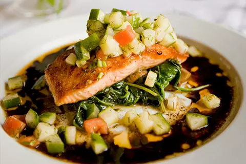 Seared salmon over greens and diced vegetables with a dark sauce