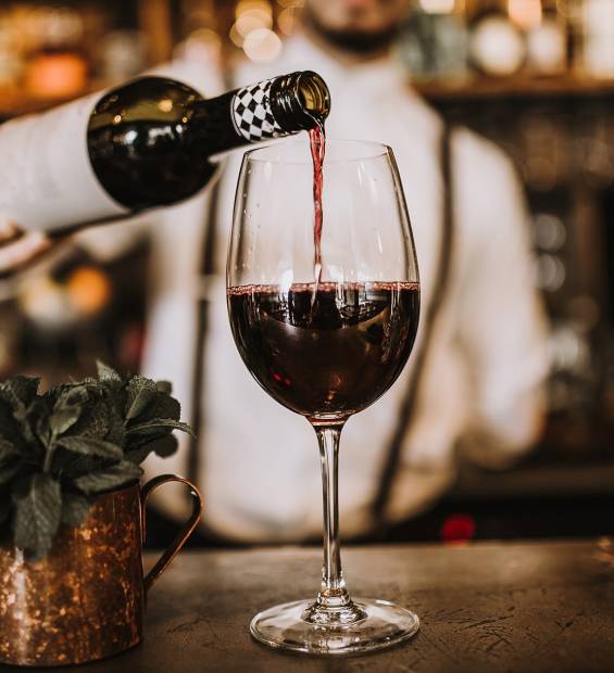 Red wine being poured into a glass at the bar, beside a copper mug with fresh mint